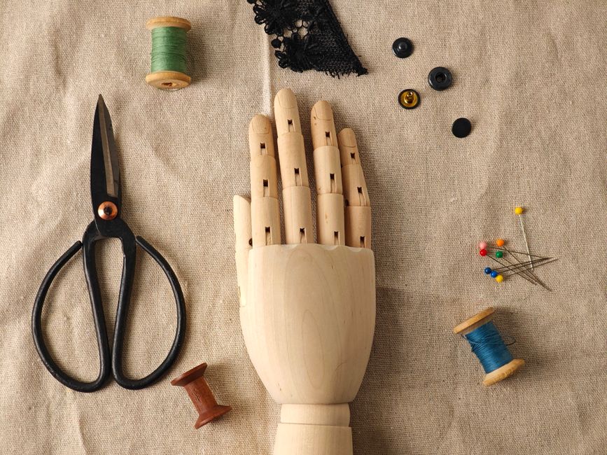 A flat lay of vintage sewing tools and a wooden hand mannequin on linen fabric.