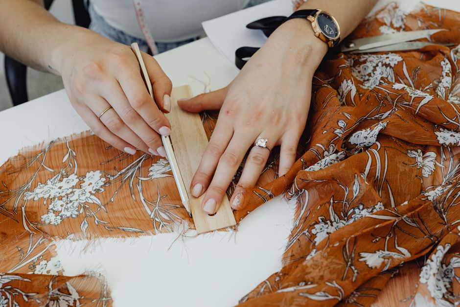 Close-up of hands expertly sewing fabric, showcasing the art of dressmaking in a workshop setting.