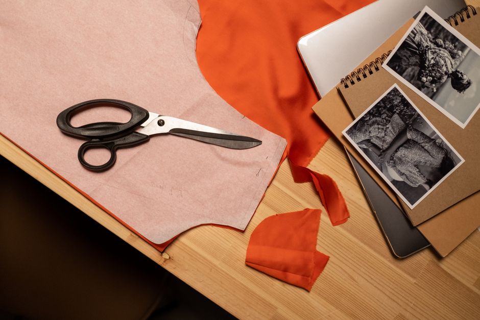 A close-up of a fashion design workspace featuring fabric, scissors, and design sketches on a table.