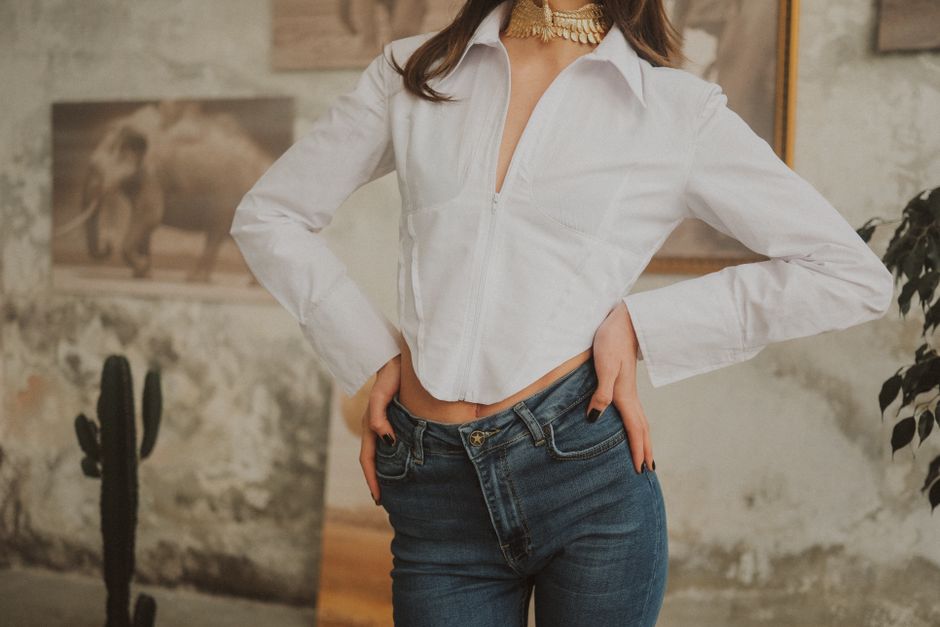 Fashionable woman posing indoors in white shirt and jeans, showcasing modern style and elegance.