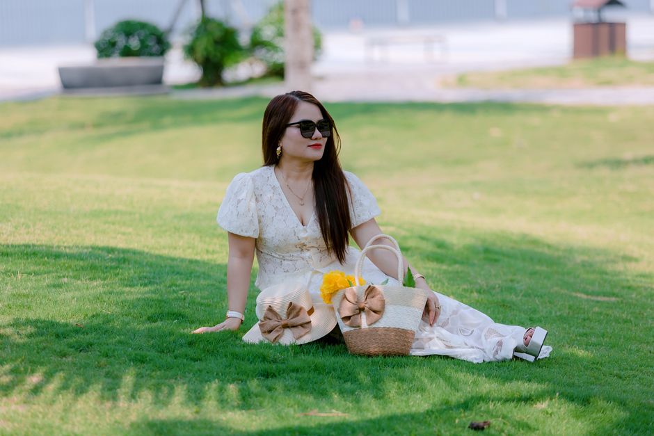 Woman in white dress sitting on grass with straw hats and baskets, enjoying a sunny day.
