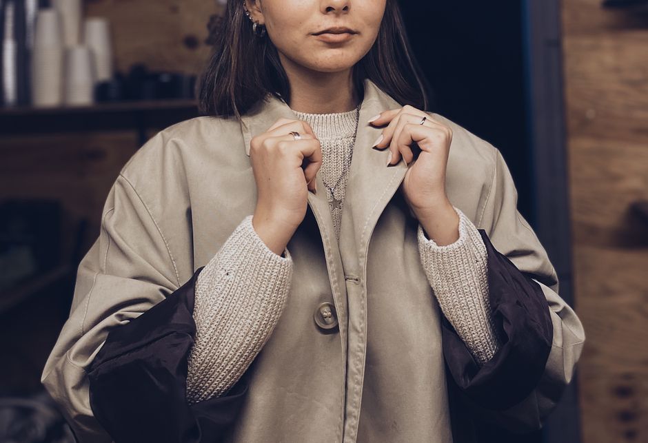 Stylish woman wearing a coat and sweater indoors, capturing a cozy fall fashion vibe.